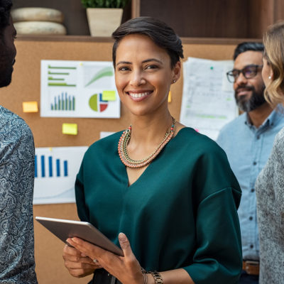 business woman looking at camera with colleagues working in background.